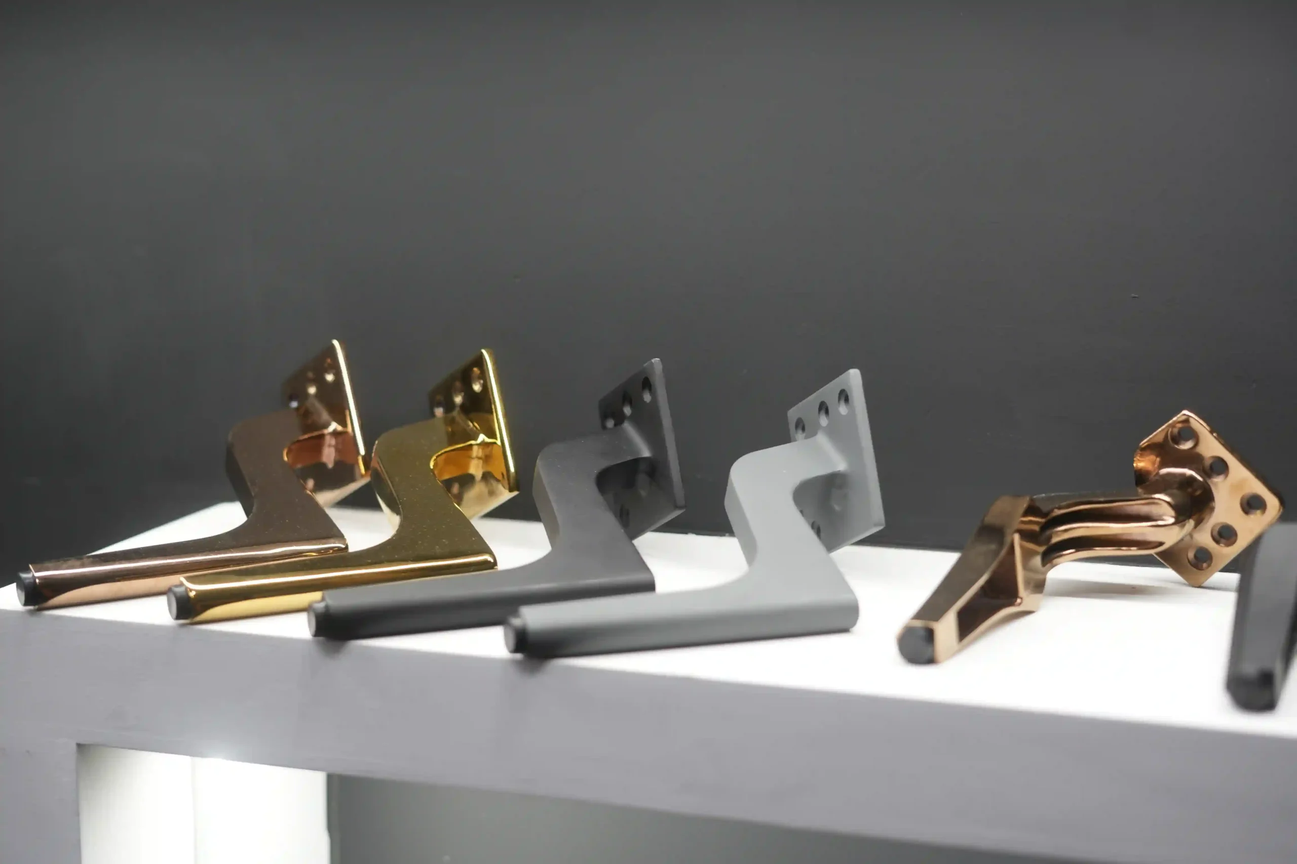 A row of furniture legs in rose gold, polished gold, matte black, graphite and copper PVD finishes