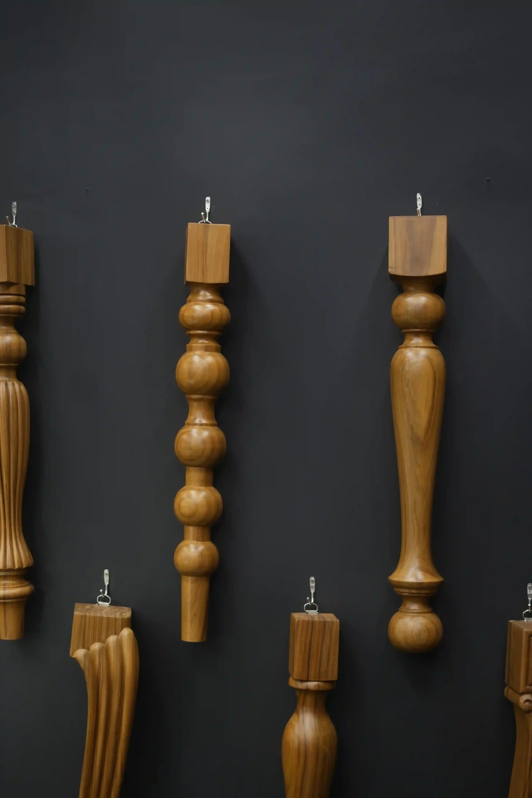 turned wooden table legs mounted vertically on a matte black display wall